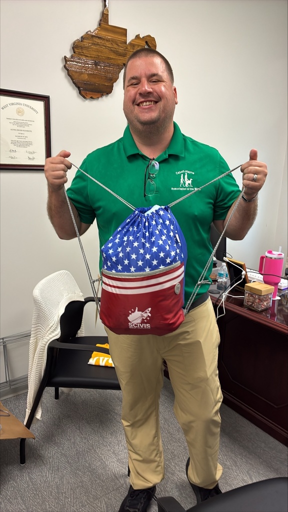A smiling man in a green Cabell-Wayne Association of the Blind polo holds a red, white and blue SCIVIS drawstring bag featuring stars, stripes and the SCIVIS logo.
