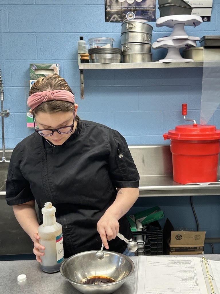 Student in a black chef uniform measures ingredients into a mixing bowl while following a recipe in the Appalachia Provisions kitchen.