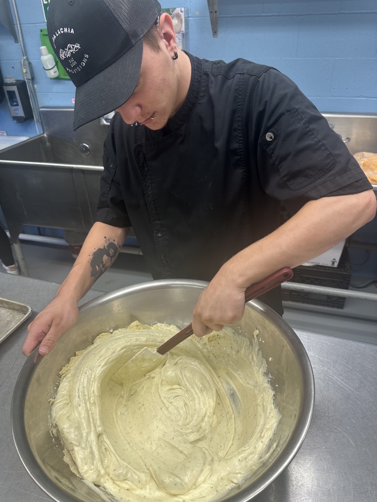 Student in an Appalachia Provisions chef uniform whisks ingredients together in a large mixing bowl.