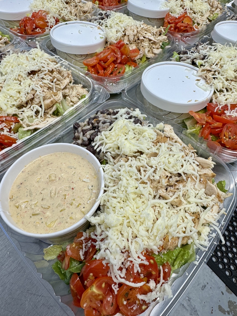 Prepared Mexican street corn chicken salads with lettuce, tomatoes, chicken, cheese, black beans and rice, with dressing on the side.