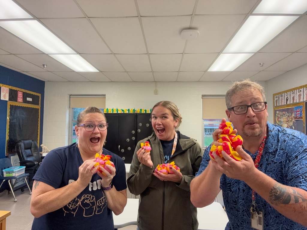 Three staff members excitedly pose with several “I Love You” ducks gathered during the campus duck hunt.