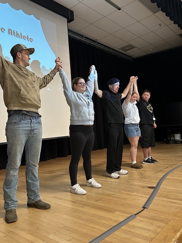 JJ Jones stands on stage between four WVSDB participants as the group holds hands and raises their arms.