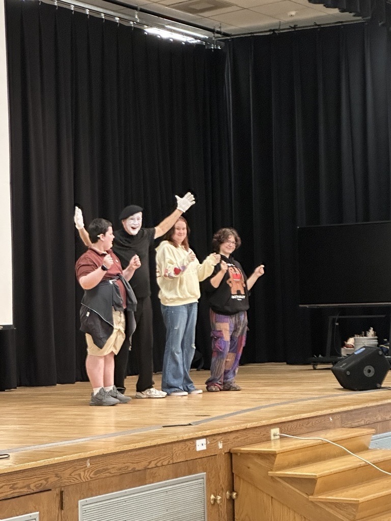JJ Jones smiles with his arms raised while standing on stage with three WVSDB participants after an activity.