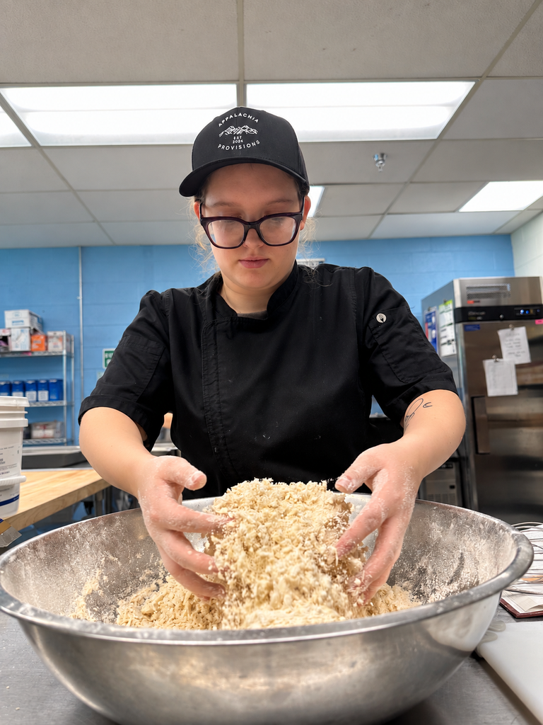 A culinary student works with ingredients in a large mixing bowl as part of hands-on food preparation at Appalachia Provisions.