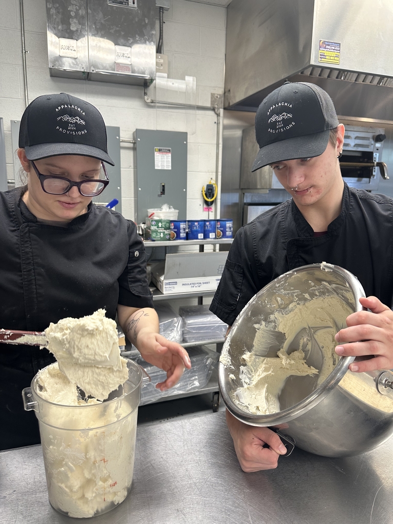 Two Appalachia Provisions culinary students work together to transfer a prepared filling from a mixing bowl in the kitchen.