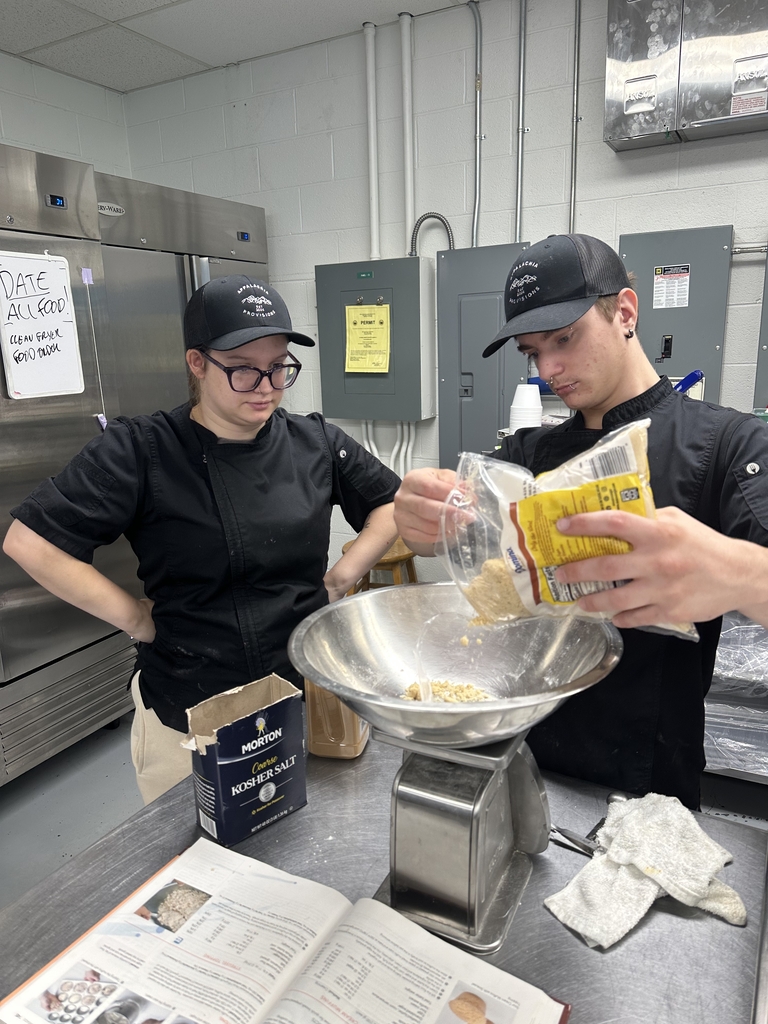 Two culinary students measure and combine ingredients using a kitchen scale during food preparation at Appalachia Provisions.