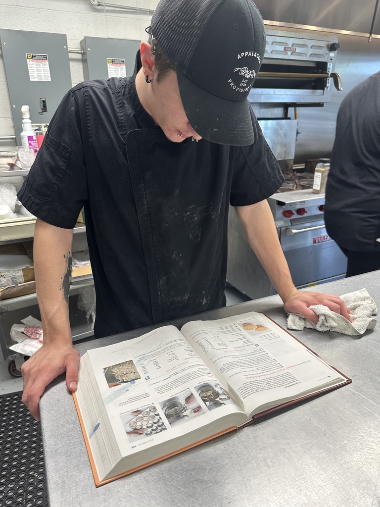 An Appalachia Provisions culinary student references a cookbook while preparing food in the kitchen.