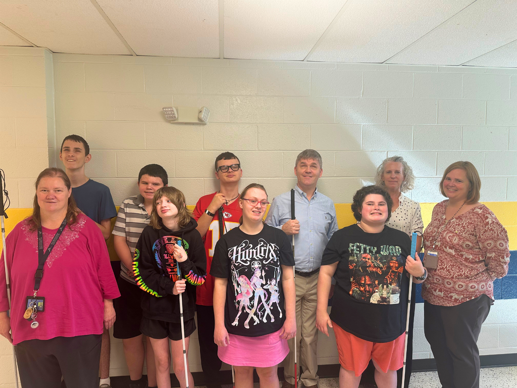 Group of WVSDB students and staff smiling together in a school hallway. Several students hold white canes.