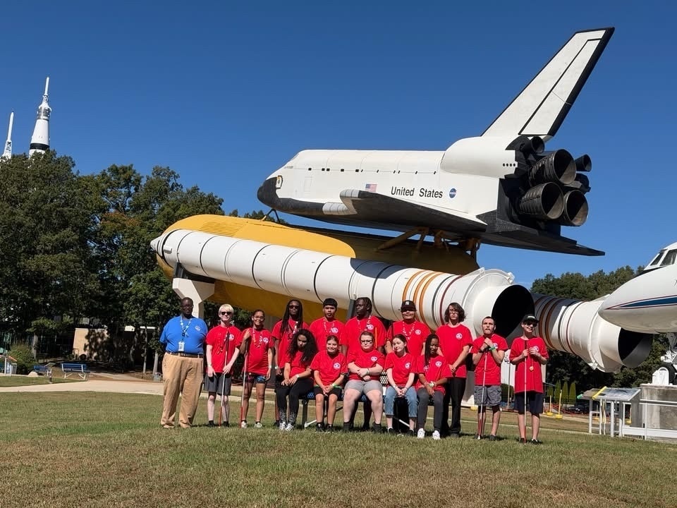 WVSDB students and staff pose together outdoors in front of a large Space Shuttle display at Space Camp.