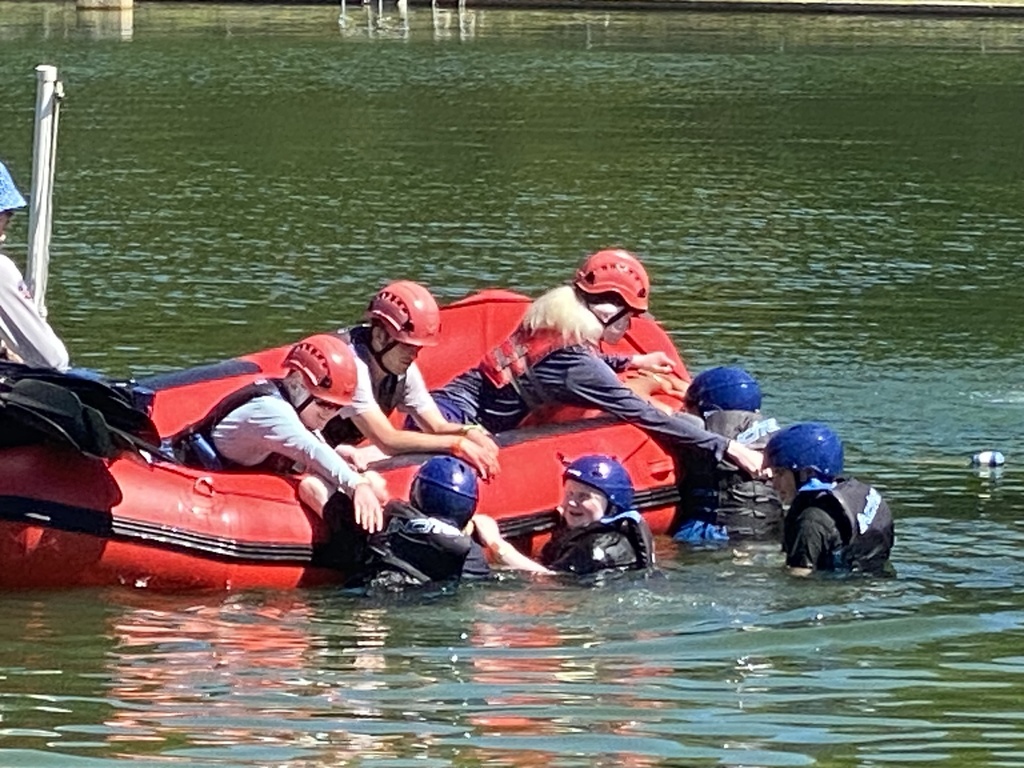 Students wearing helmets and safety gear work together around a raft during a water-based Space Camp activity.