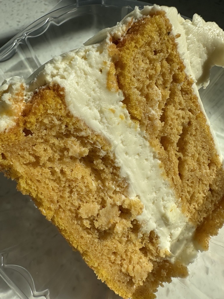 Close-up of a slice of pumpkin roll layer cake with layers of pumpkin cake and creamy white frosting.
