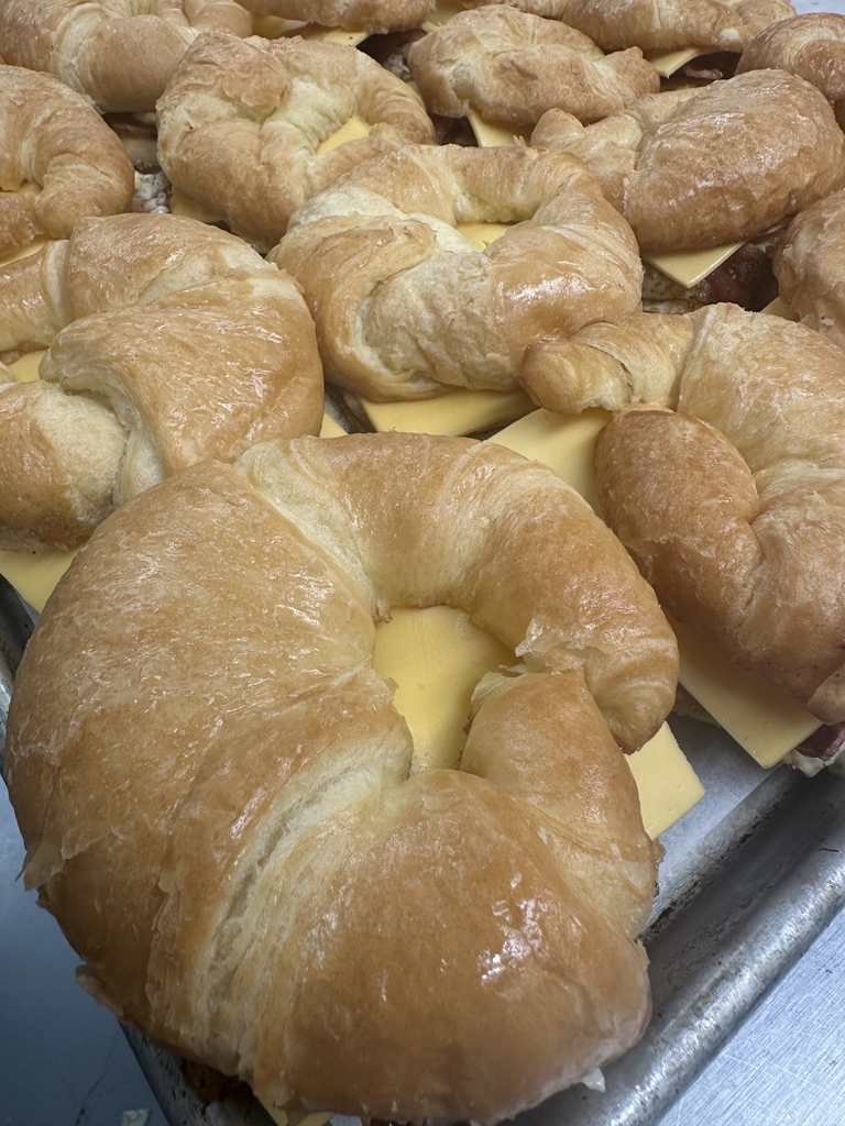 Freshly prepared croissant sandwiches filled with cheese and meat, arranged together on a tray.
