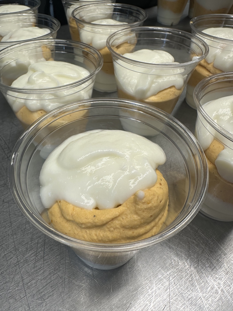 Individual cups of pumpkin dessert layered with a creamy white topping, arranged on a stainless steel countertop.