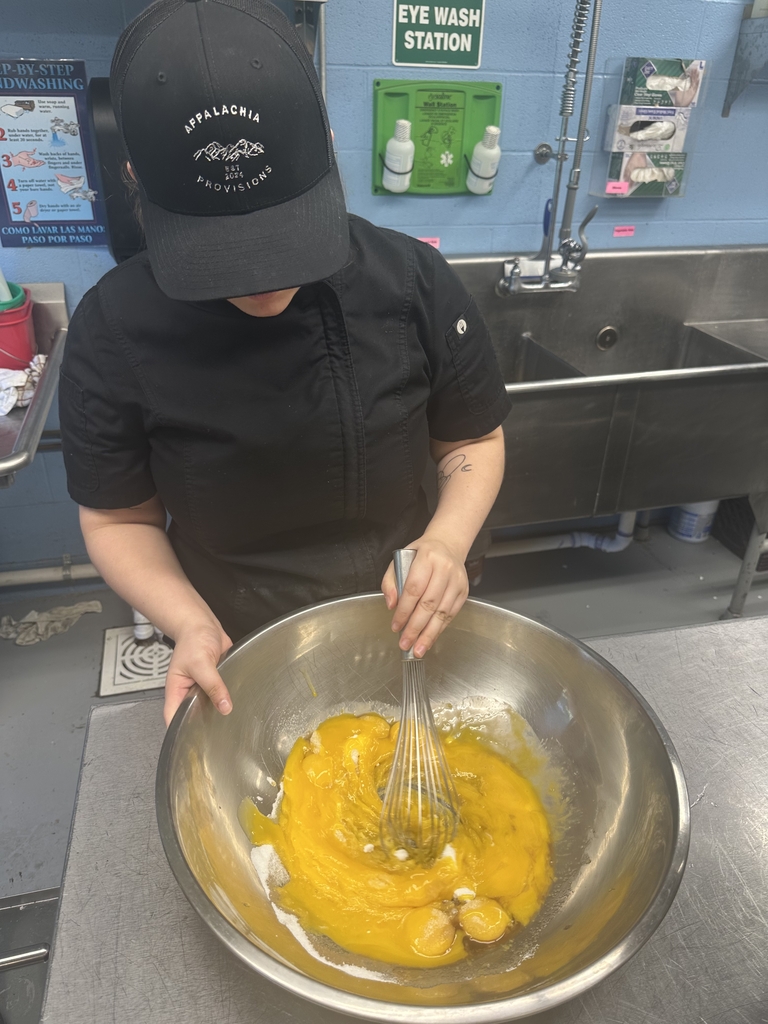 A culinary student wearing an Appalachia Provisions hat whisks ingredients in a large stainless steel mixing bowl in the kitchen.