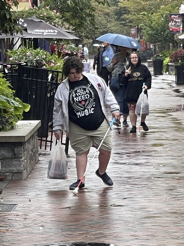 WVSDB Blind/Low Vision students use white mobility canes while traveling along a wet downtown sidewalk in Winchester, Virginia, during an Orientation & Mobility lesson.