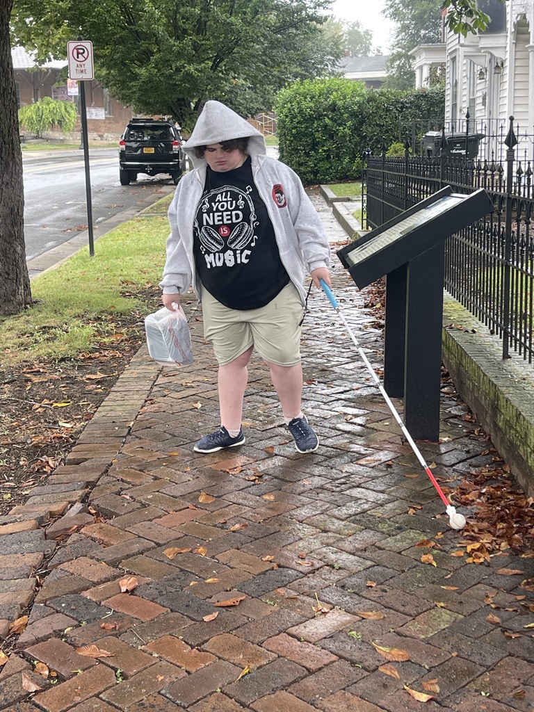 A WVSDB Blind/Low Vision student uses a white mobility cane to navigate a wet brick sidewalk in Winchester during an Orientation & Mobility lesson.