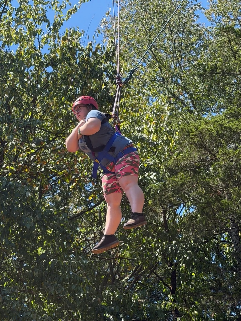 WVSDB student wearing a helmet and safety harness suspended in the air during an outdoor challenge course activity.