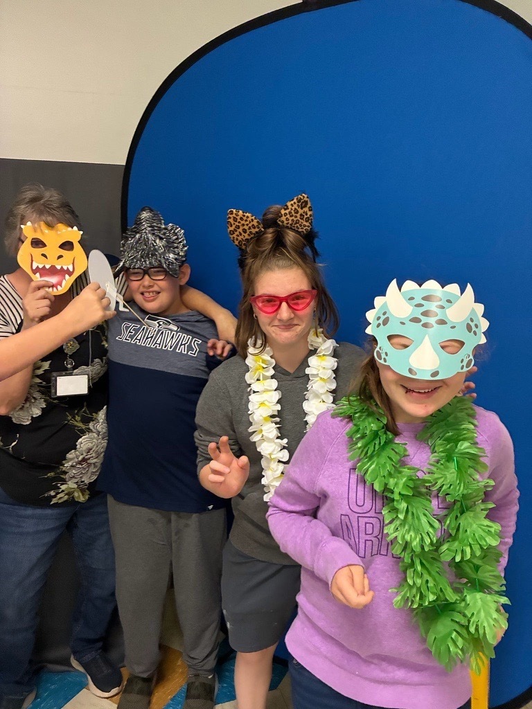 Four individuals pose together wearing playful photo booth accessories, including animal masks, leopard-print ears, colorful glasses, and feather leis.