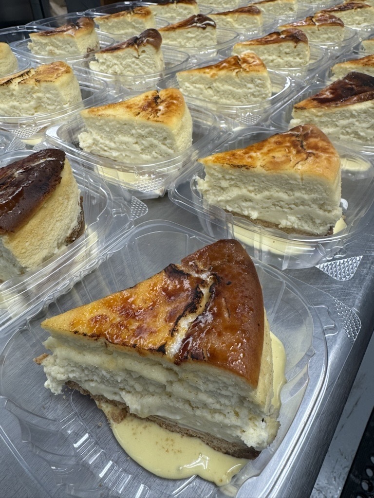 Individual slices of crème brûlée cheesecake with caramelized tops are arranged in clear takeout containers.