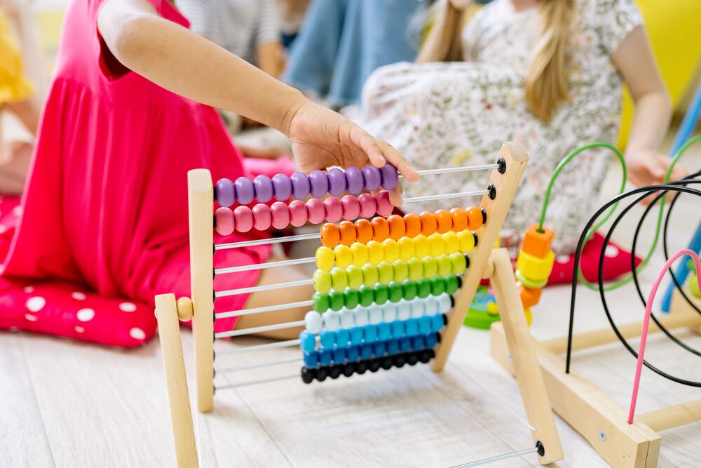 Image of a rainbow colored toy abacus and two girl toddlers playing