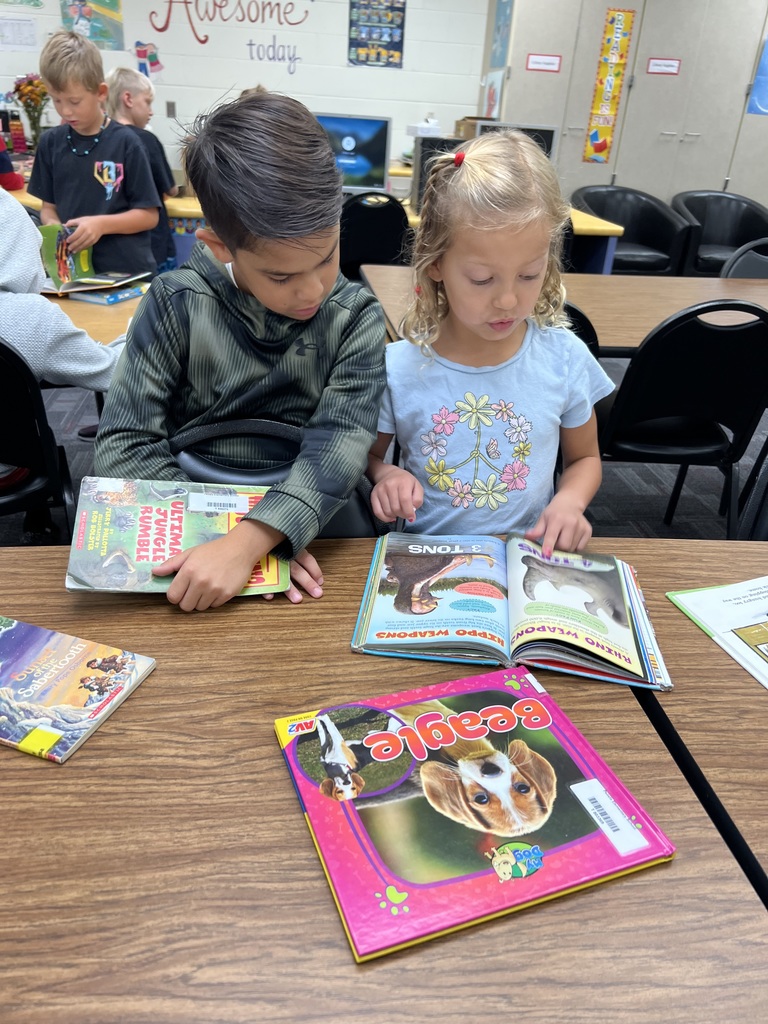 Two students reading books together at classroom table.