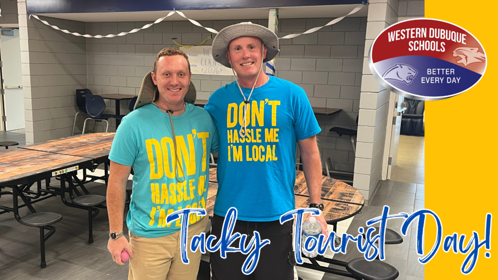 Two staff members smile in a cafeteria while wearing wide-brimmed hats and matching bright blue shirts with the phrase “Don’t Hassle Me I’m Local” in large yellow letters. The graphic text reads “Tacky Tourist Day!” with the Western Dubuque Schools logo in the corner.