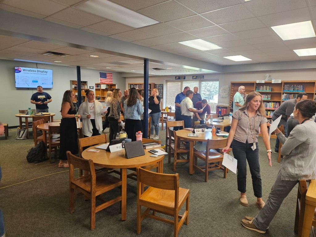 Adults standing and conversing in small groups in a library during a workshop session