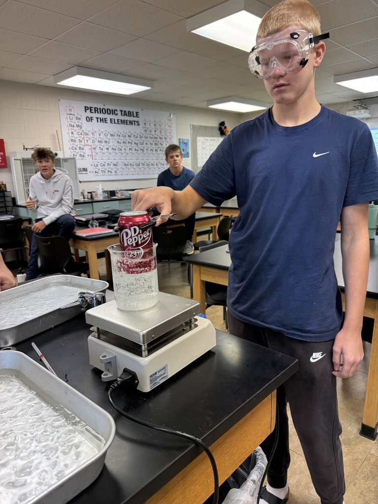 Student in goggles watching a Dr. Pepper can reaction on a hot plate.