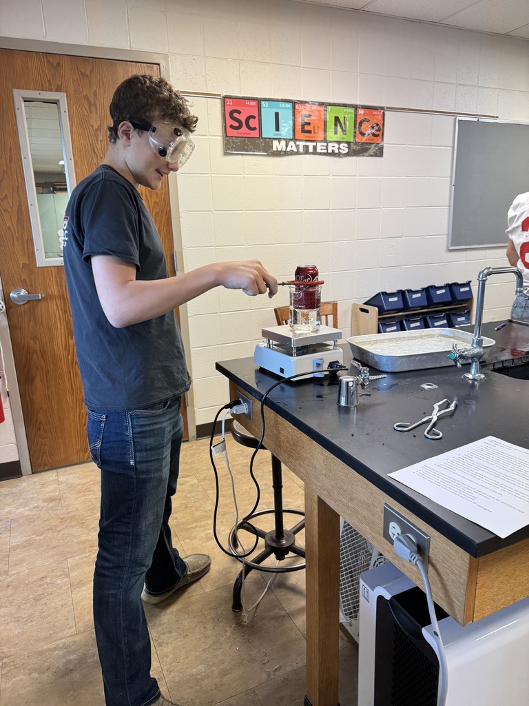 Smiling student in goggles conducting a Dr. Pepper can lab experiment.
