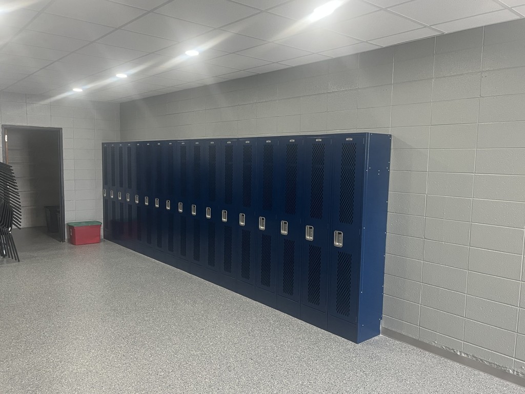 Row of new blue metal lockers against a gray wall in a brightly lit hallway with polished gray speckled flooring.