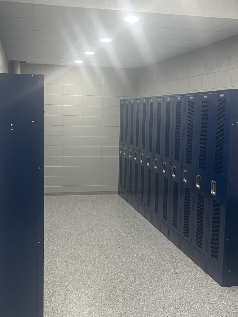 Narrow hallway view showing two rows of blue metal lockers facing each other under ceiling lights.