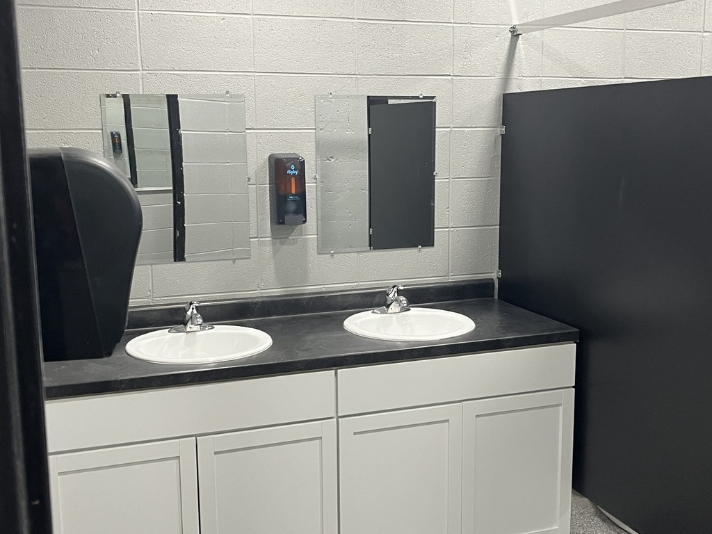 Restroom area with two white sinks set in a black countertop, mirrors above, and a soap dispenser on the wall.