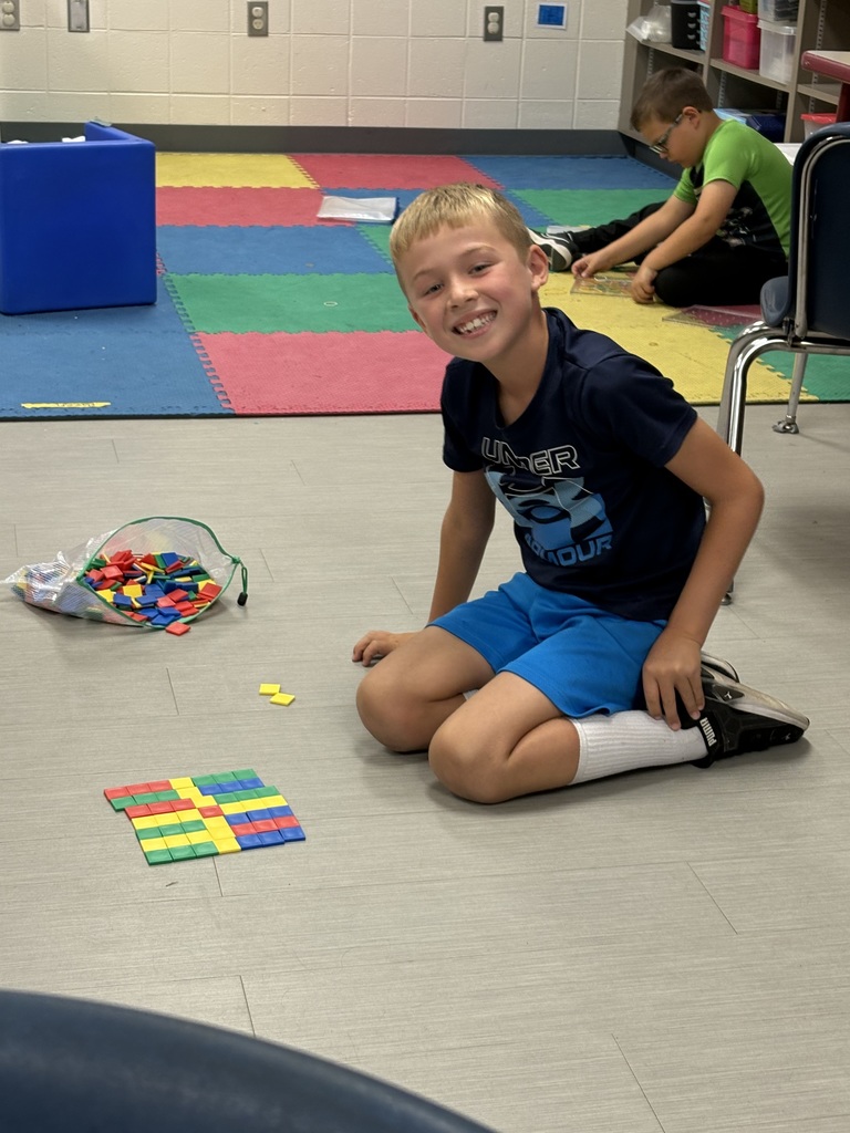 Smiling student sits on the classroom floor building a colorful square design with plastic tiles.