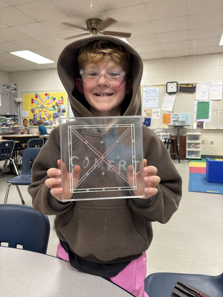 Student wearing glasses and a hoodie holds up a clear geoboard with rubber bands stretched into geometric shapes