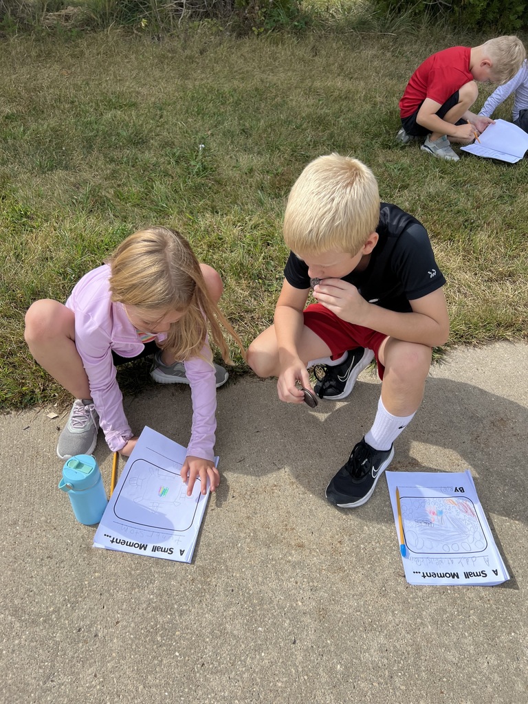 A girl and boy sit together with notebooks and worksheets on the ground. The boy eats an Oreo while the girl points to her work.