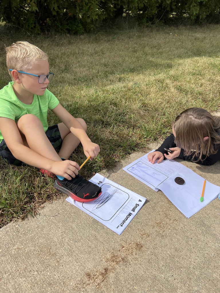 Two students sit on the sidewalk with notebooks and pencils. An Oreo cookie rests on the page as part of their outdoor activity.