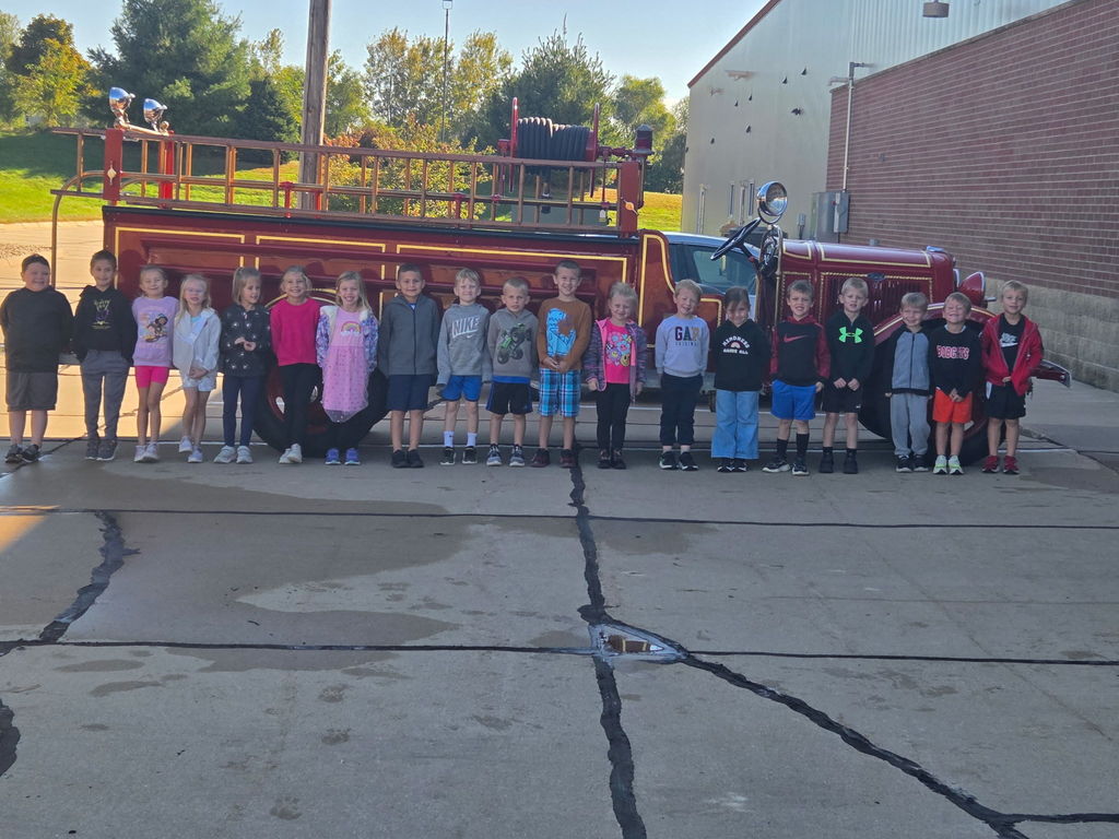 A group of students stand outdoors in front of an old fire truck.