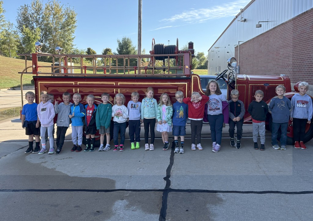A group of students stand outdoors in front of an old fire truck.