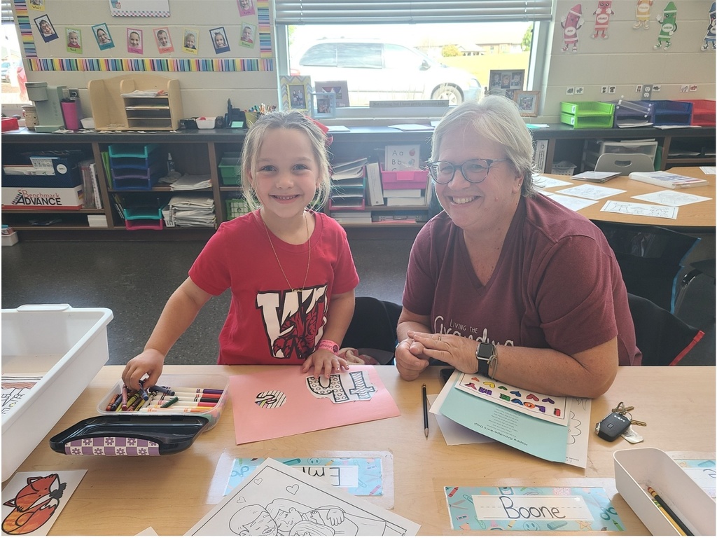Student engaging in a cut and glue project with her grandparent sitting beside her. 