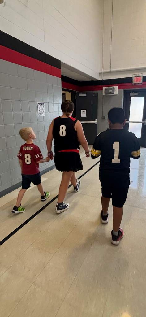 Three children walking down a hallway wearing sports jerseys with numbers 8, 8, and 1.