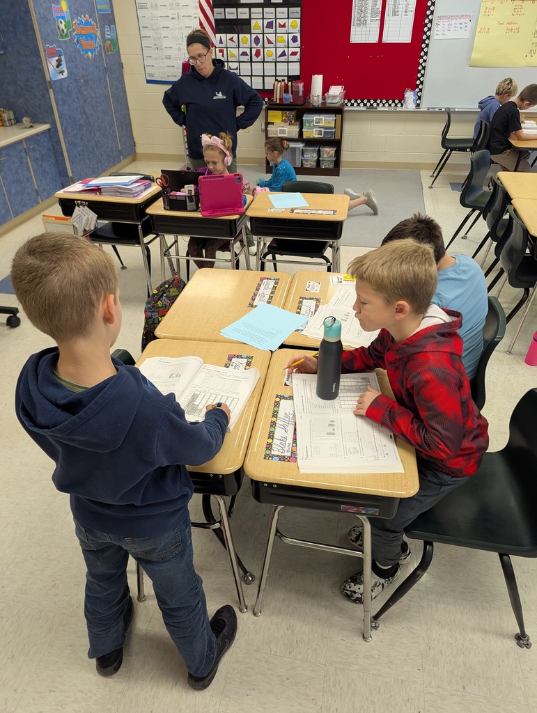 Students work together at desks on math assignments while a teacher observes nearby.
