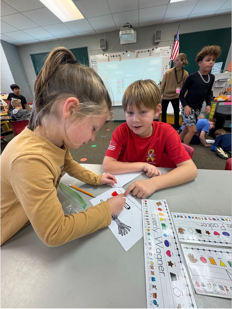 Two students work together on a fall-themed worksheet at their classroom table.