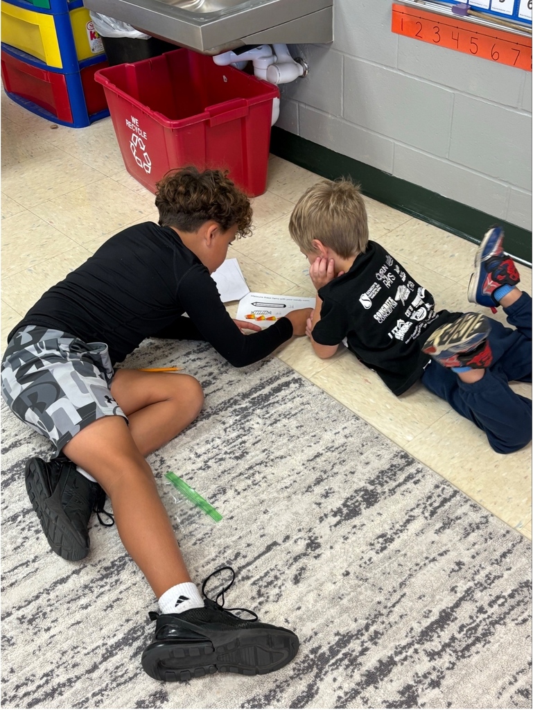 Two students lie on the classroom floor collaborating on a worksheet that includes candy corn illustrations.