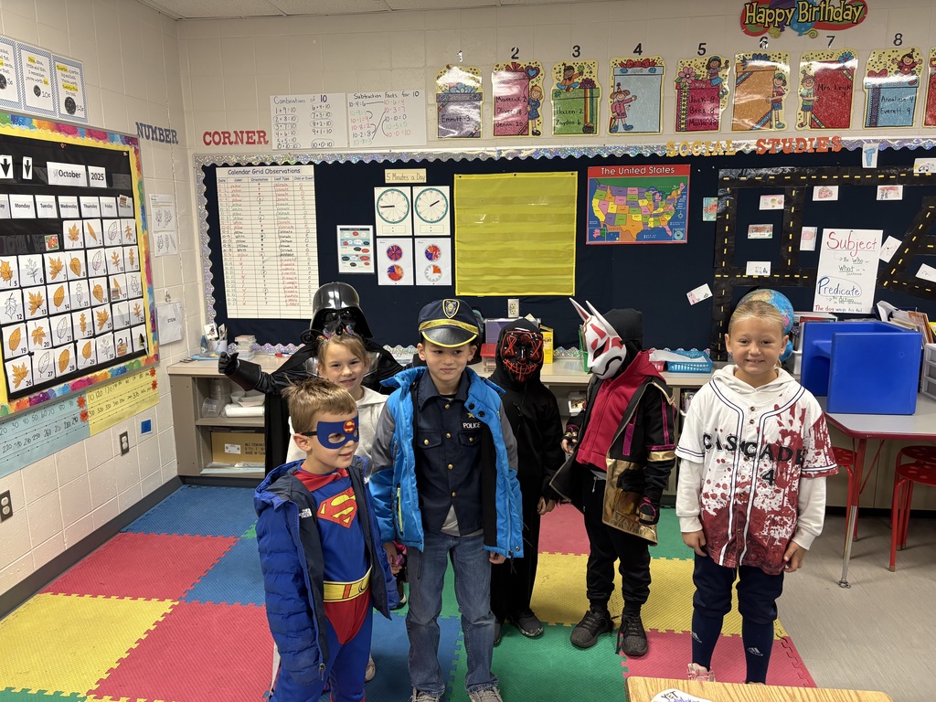 Seven elementary students stand together in costume, featuring characters such as Superman, Darth Vader, a police officer, and a baseball player.