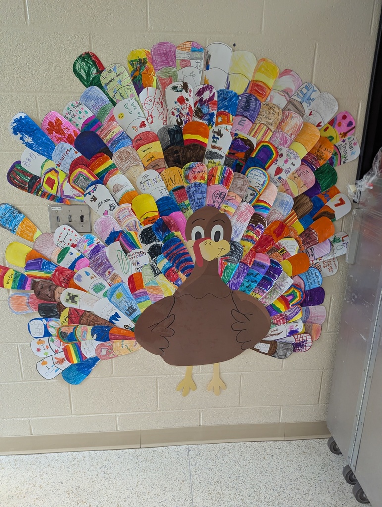 A large paper turkey displayed on a school hallway wall, with colorful hand-drawn feathers created by students.