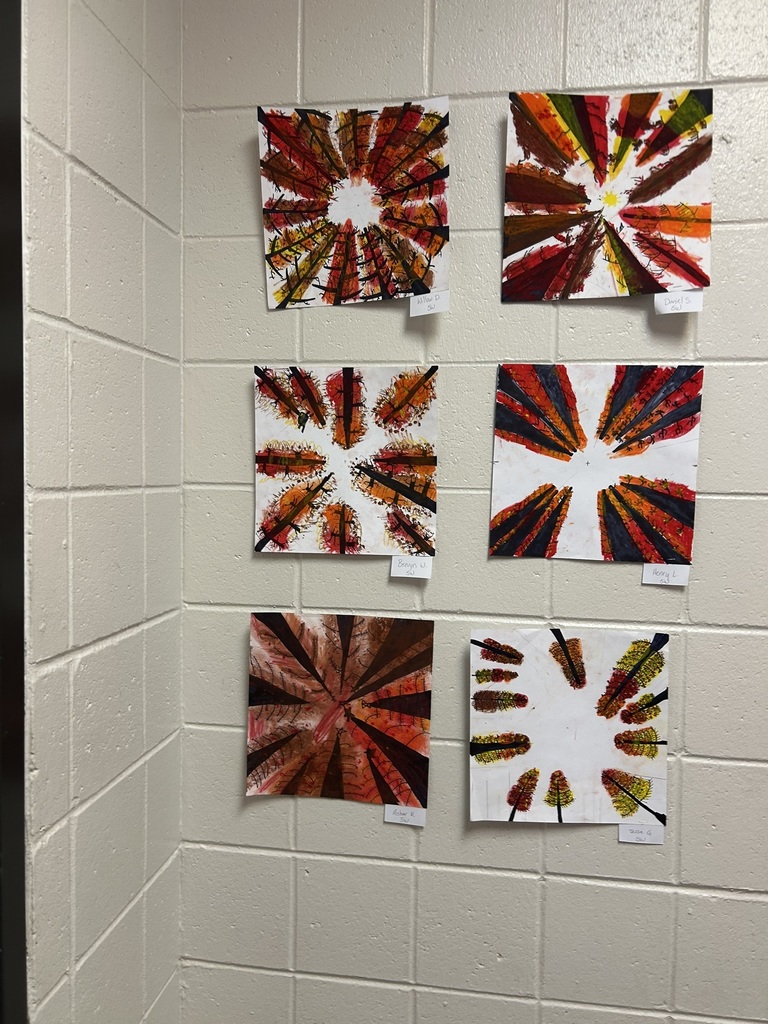 Six square pieces of student radial artwork with fall colors displayed on a white tiled wall, each labeled with a student’s name.