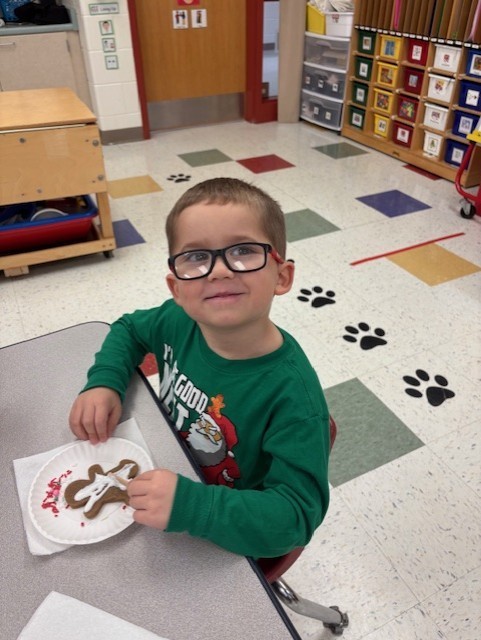 Young students participate in a festive classroom activity, decorating and baking gingerbread cookies using rolling pins, icing, and toppings.