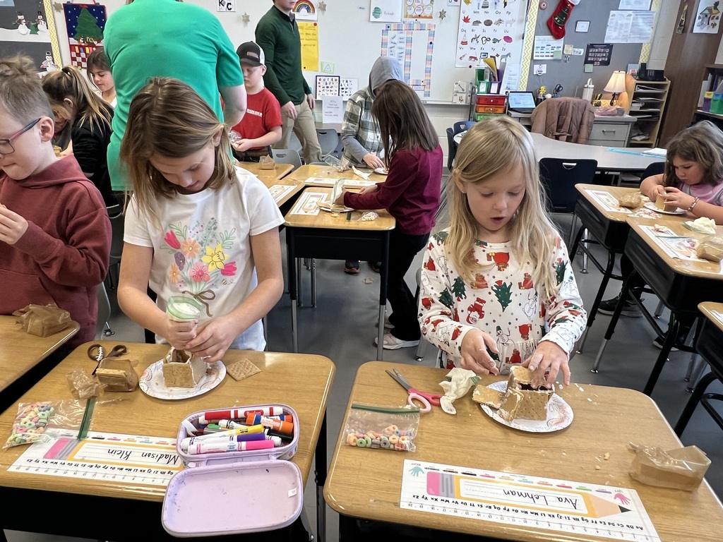 Two girls work intently on decorating graham cracker houses with frosting at their desks