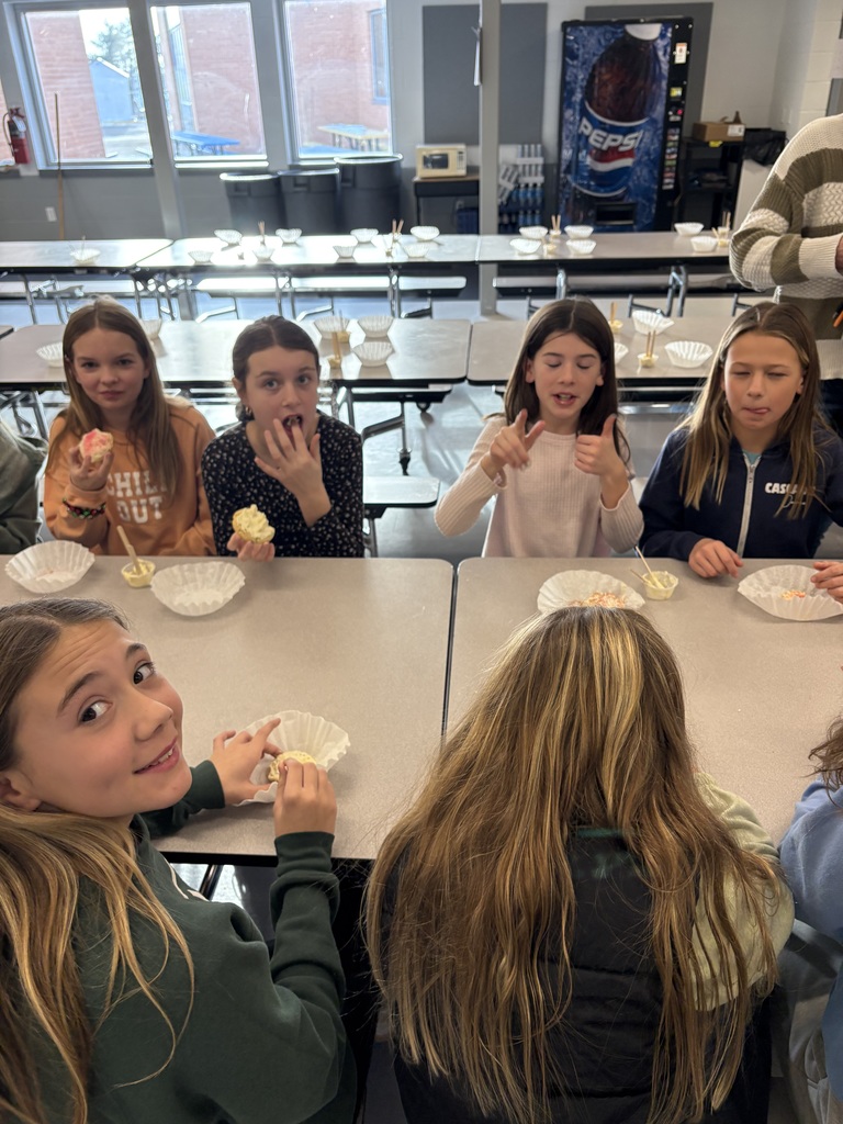 Girls sit at a cafeteria table, smiling and eating cookies they decorated with colorful frosting and sprinkles.