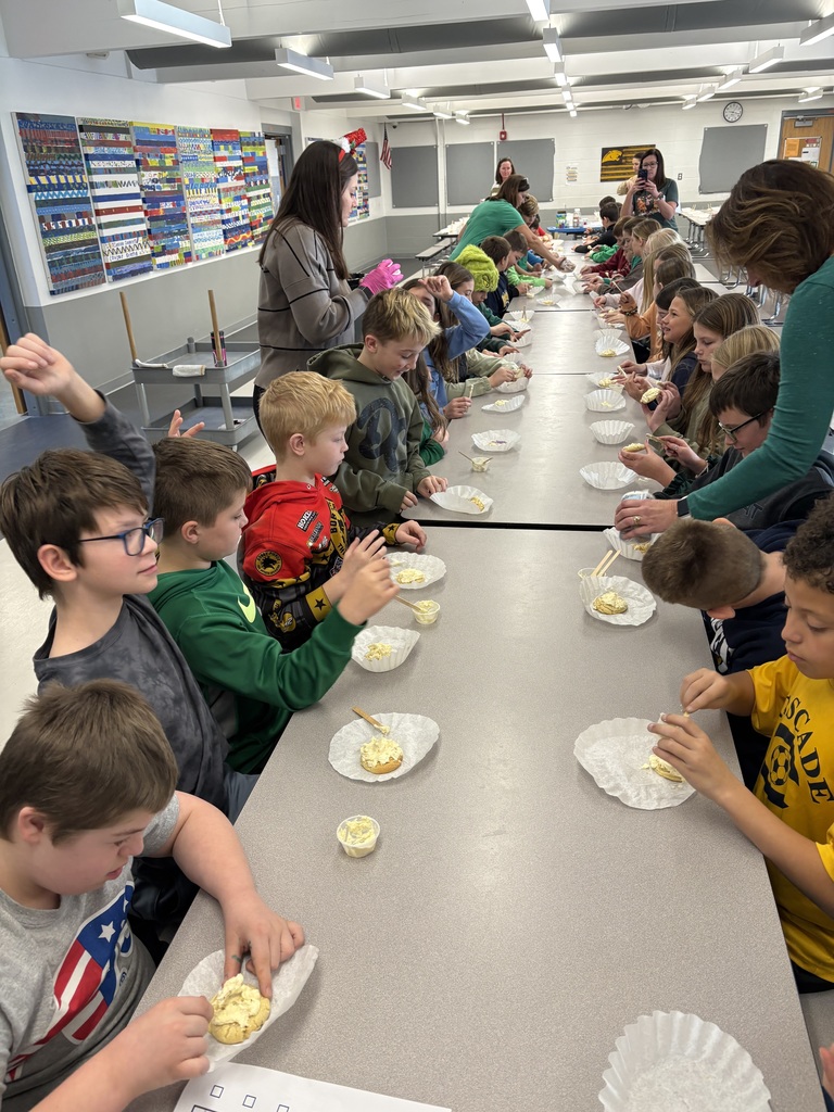 A long row of students decorates cookies at cafeteria tables while teachers assist during a festive classroom activity.